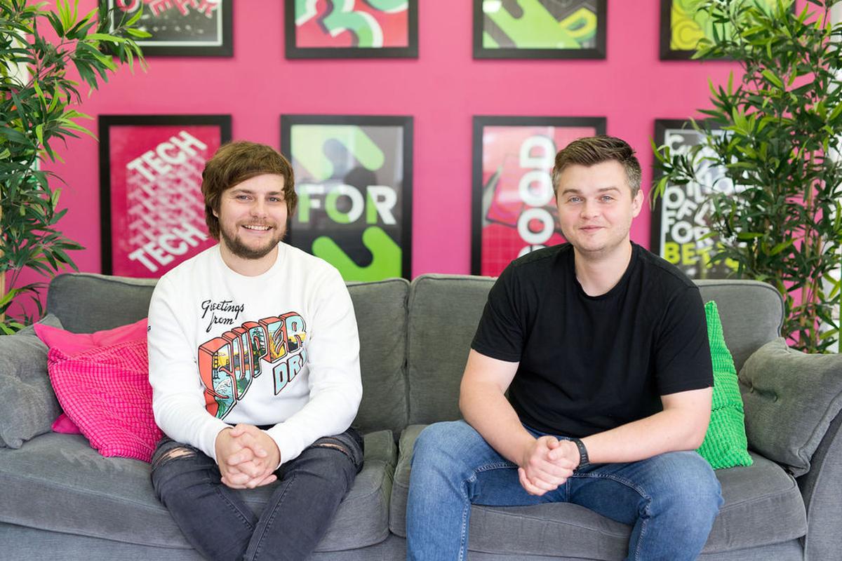 Kev and Tom smiling for a photo. They are sat next to each other on a sofa in the office.