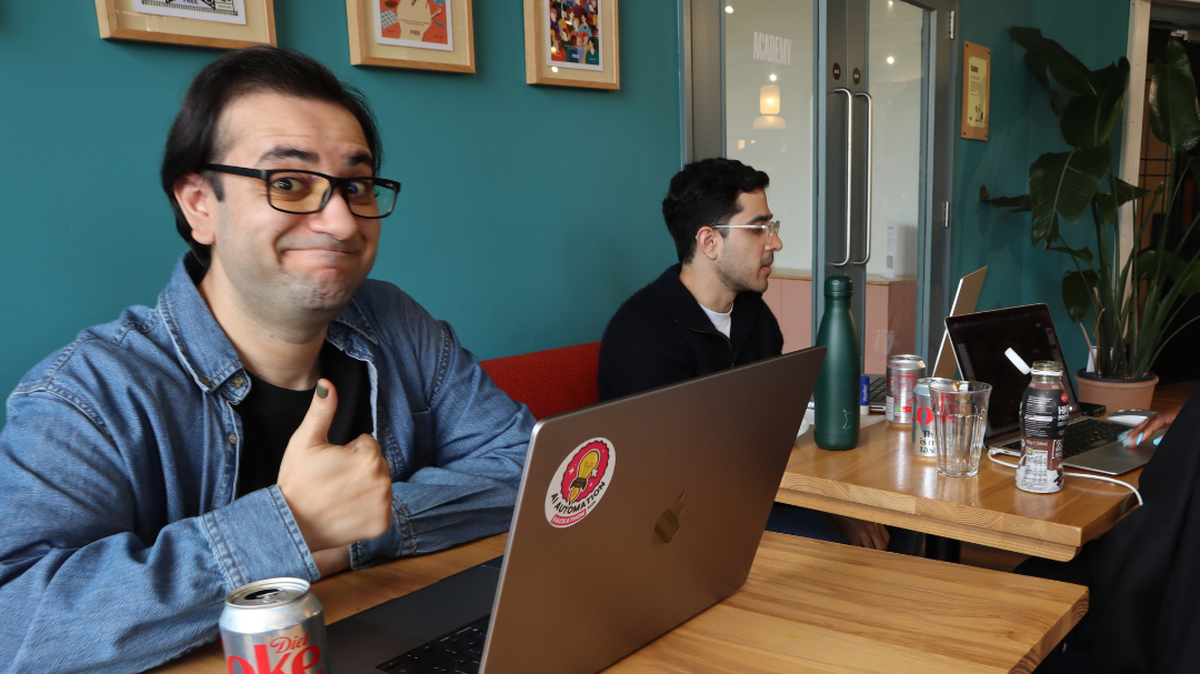Two people working on laptops at a table, one giving a thumbs up.