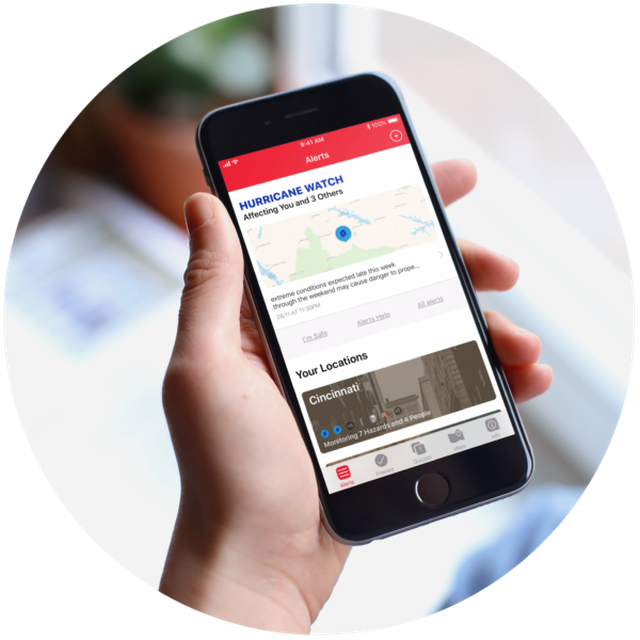 Hand holding a mobile device with an app open displaying hurricane warning pins on a map